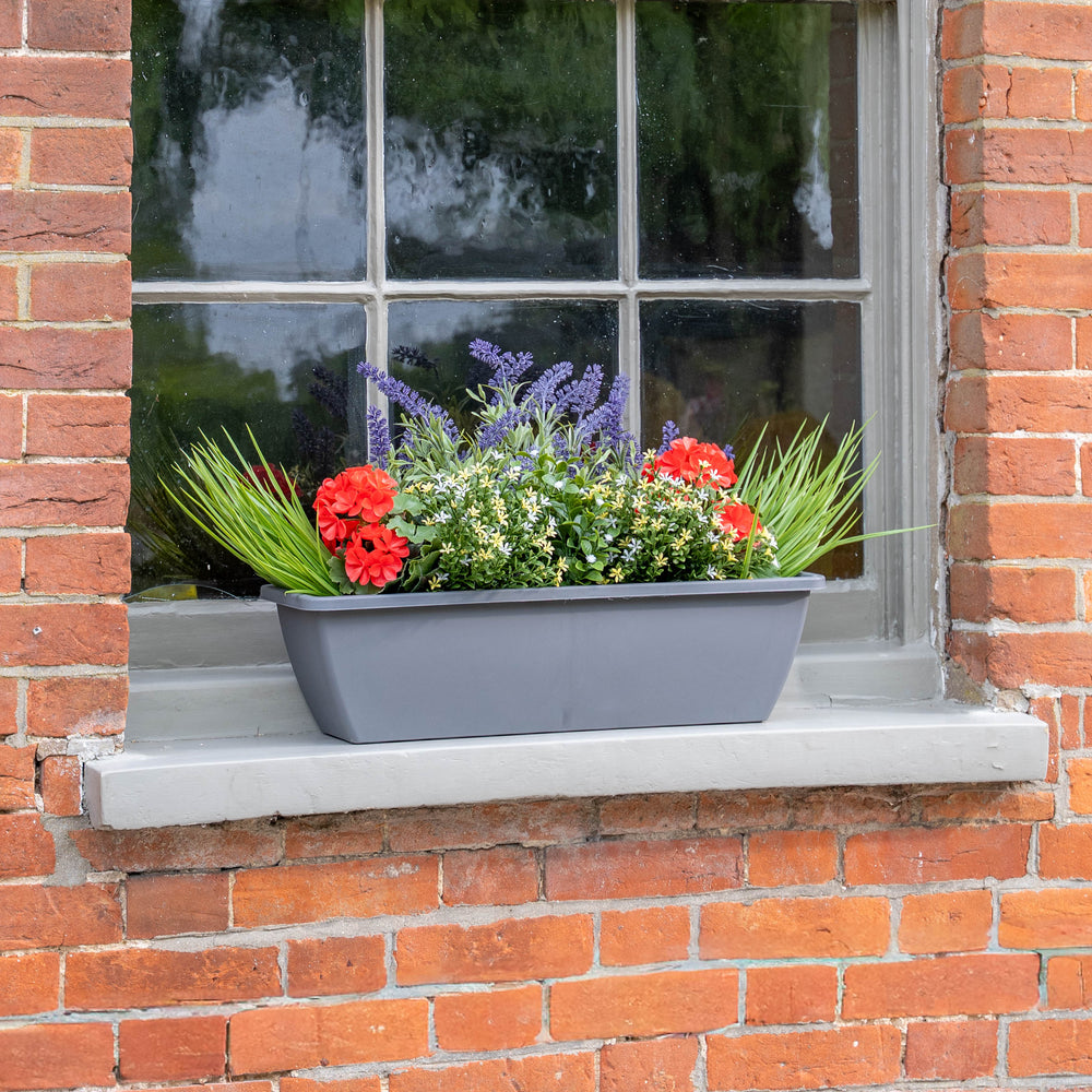 Window box with red, purple and yellow flowers with some grass greenery on a brick wall