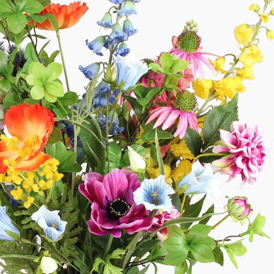 A dense arrangement of artificial wildflowers with green leaves, including orange, pink, yellow, blue and purple, set against a plain white background.