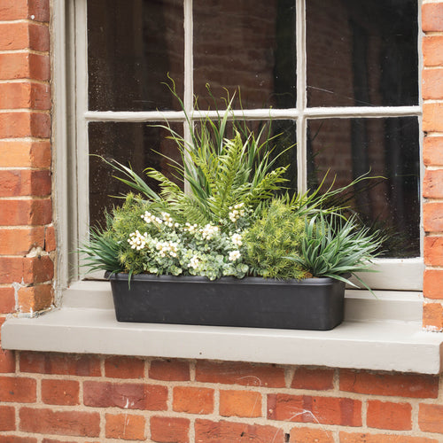 Windowsill with a black planter containing green plants on a red brick wall.