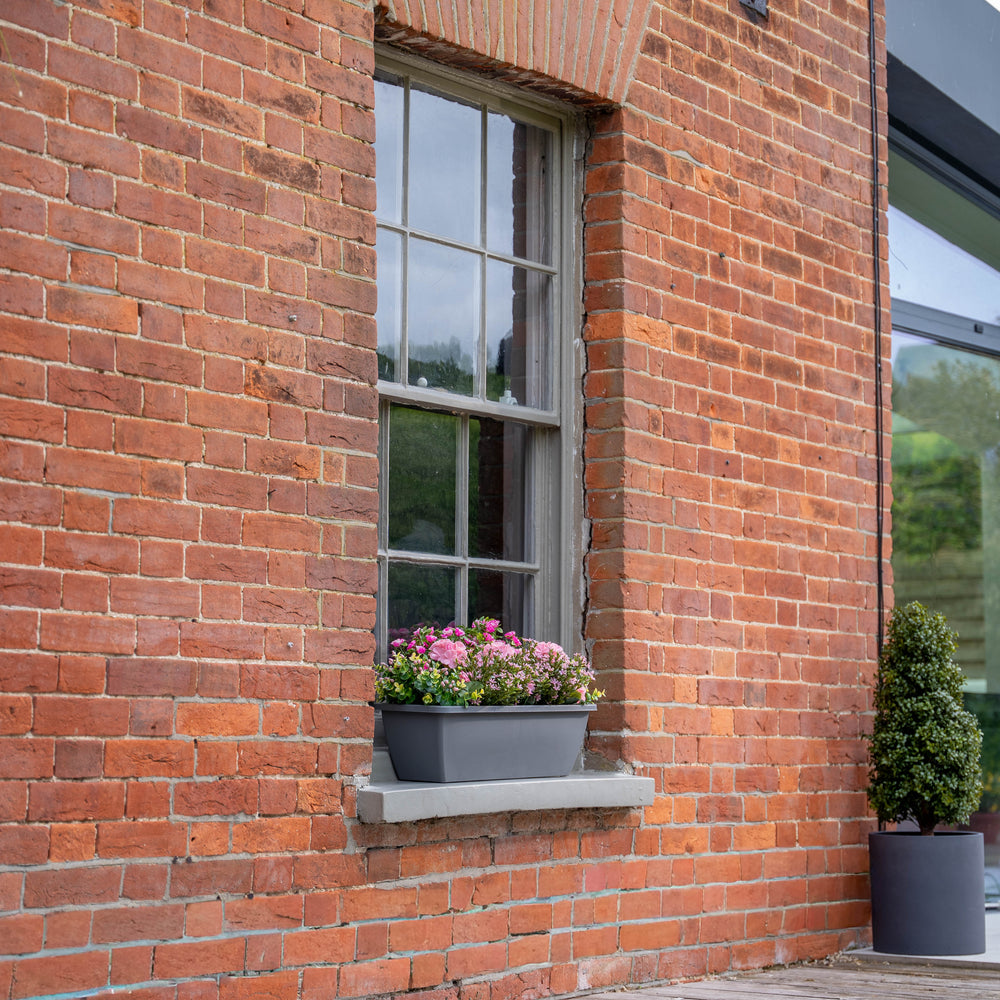 Brick building with a window box of pink flowers.