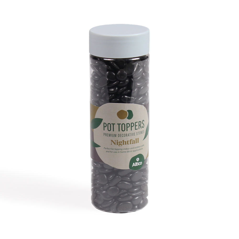 A tall, clear plastic jar filled with glossy black decorative stones, featuring a white lid and a cream and green colored label.