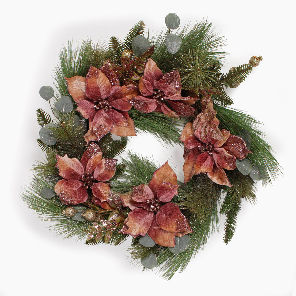 A festive holiday wreath featuring large, textured poinsettia flowers in dusty rose tones, mixed with green pine branches, eucalypts and small gold decorations on a white background.