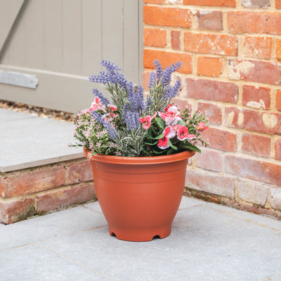 Plastic pot with colourful flowers on a patio next to a brick wall