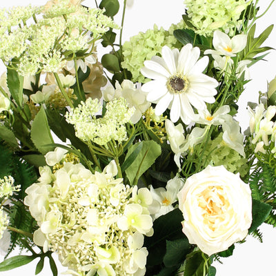 A close-up of a white and cream floral arrangement with green foliage on a white background.