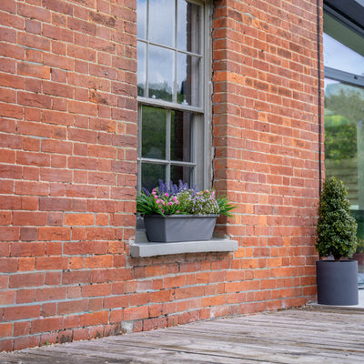 Brick building with a window box and potted plants on a wooden deck