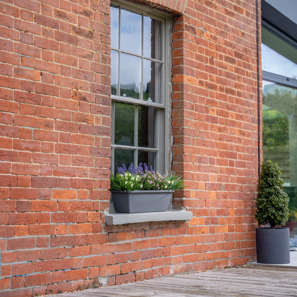 Brick building with a window box and potted plants on a wooden deck.
