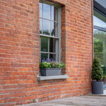 Brick building with a window box and potted plants on a wooden deck.