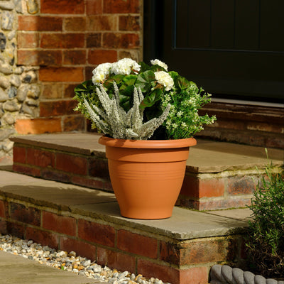 Terracotta pot with flowers on a stone step next to a brick wall.