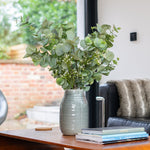 Green vase with eucalyptus on a table in a living room