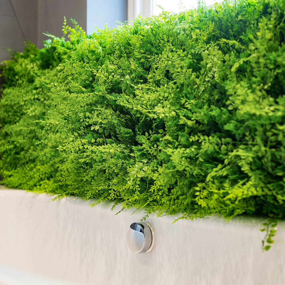 Artificial green wall panels surrounding a white bathtub.
