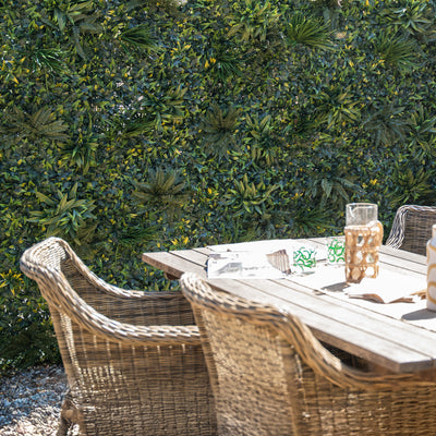Outdoor setting with wicker chairs and table against a green bush background