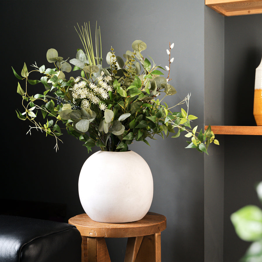 White vase with greenery on a wooden table against a dark wall