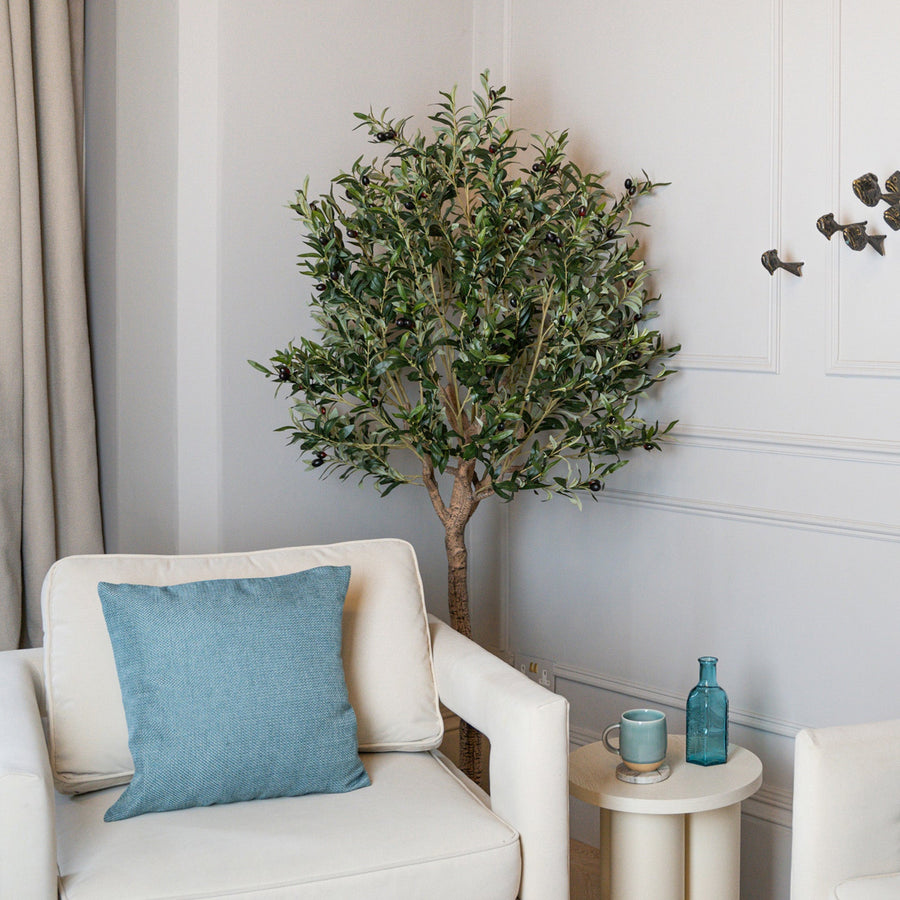 White armchair with a blue pillow and a small table with a plant and decorative items in a room.