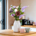White vase with flowers on a wooden table in a kitchen setting