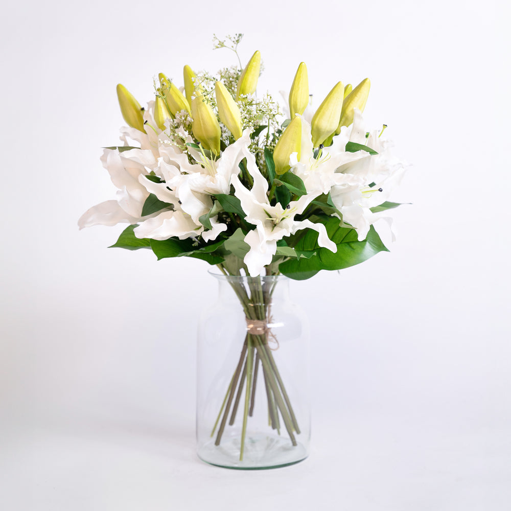 Bouquet of white and yellow flowers in a clear vase on a light gray background