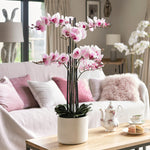 Living room with pink orchids on a coffee table, white sofa, and large windows.