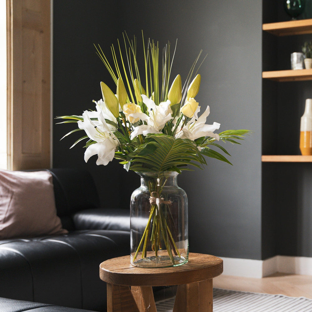 Floral arrangement in a clear vase on a wooden side table in a living room.