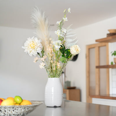 White vase with flowers on a table in a room with a blurred background