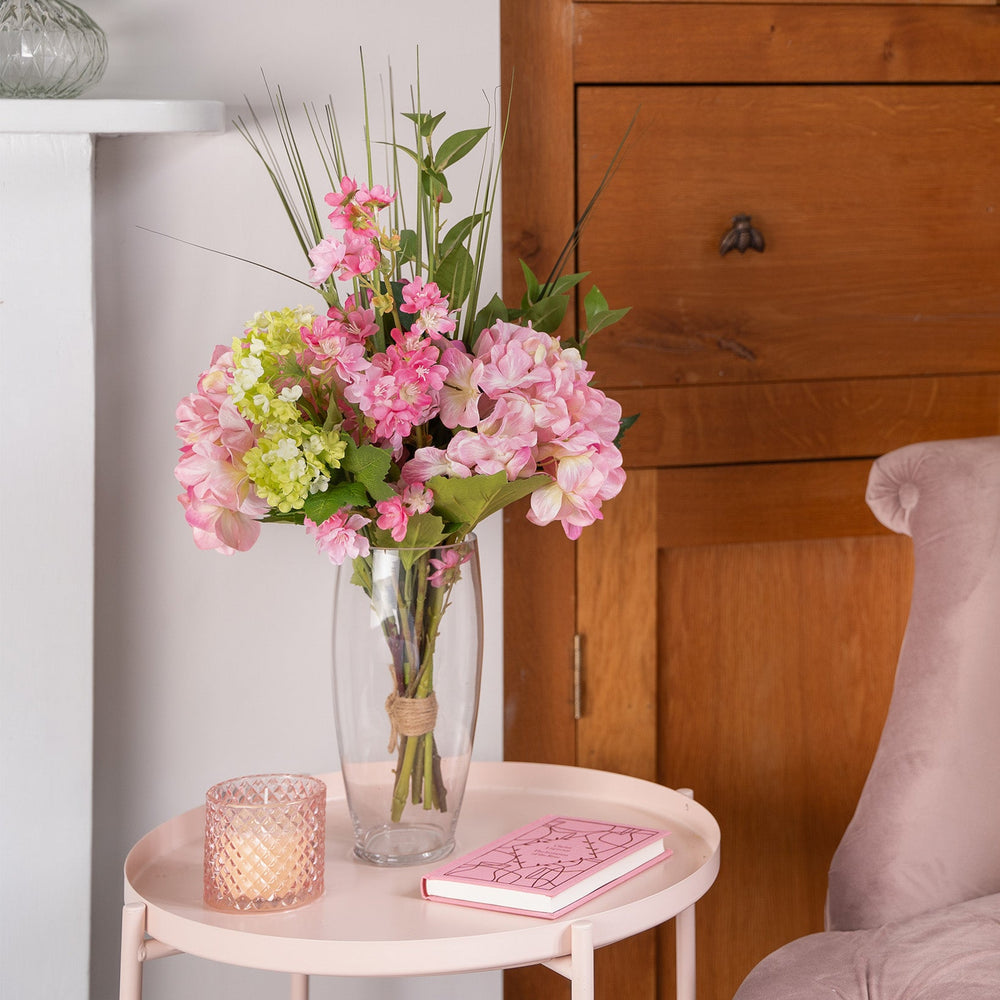 Floral arrangement in a vase on a small table next to a chair with a wooden cabinet in the background.