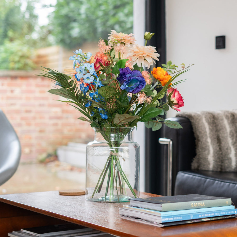 Colorful bouquet of flowers in a vase on a wooden table with a couch and window in the background