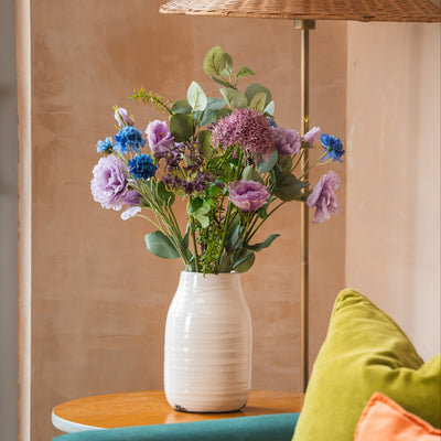 Vase with flowers on a table next to a lamp and colorful cushions on a couch.