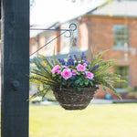 Hanging basket with flowers and ferns attached to a wooden post outdoors.