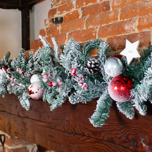 Decorative Christmas garland with ornaments on a wooden mantel against a brick wall.