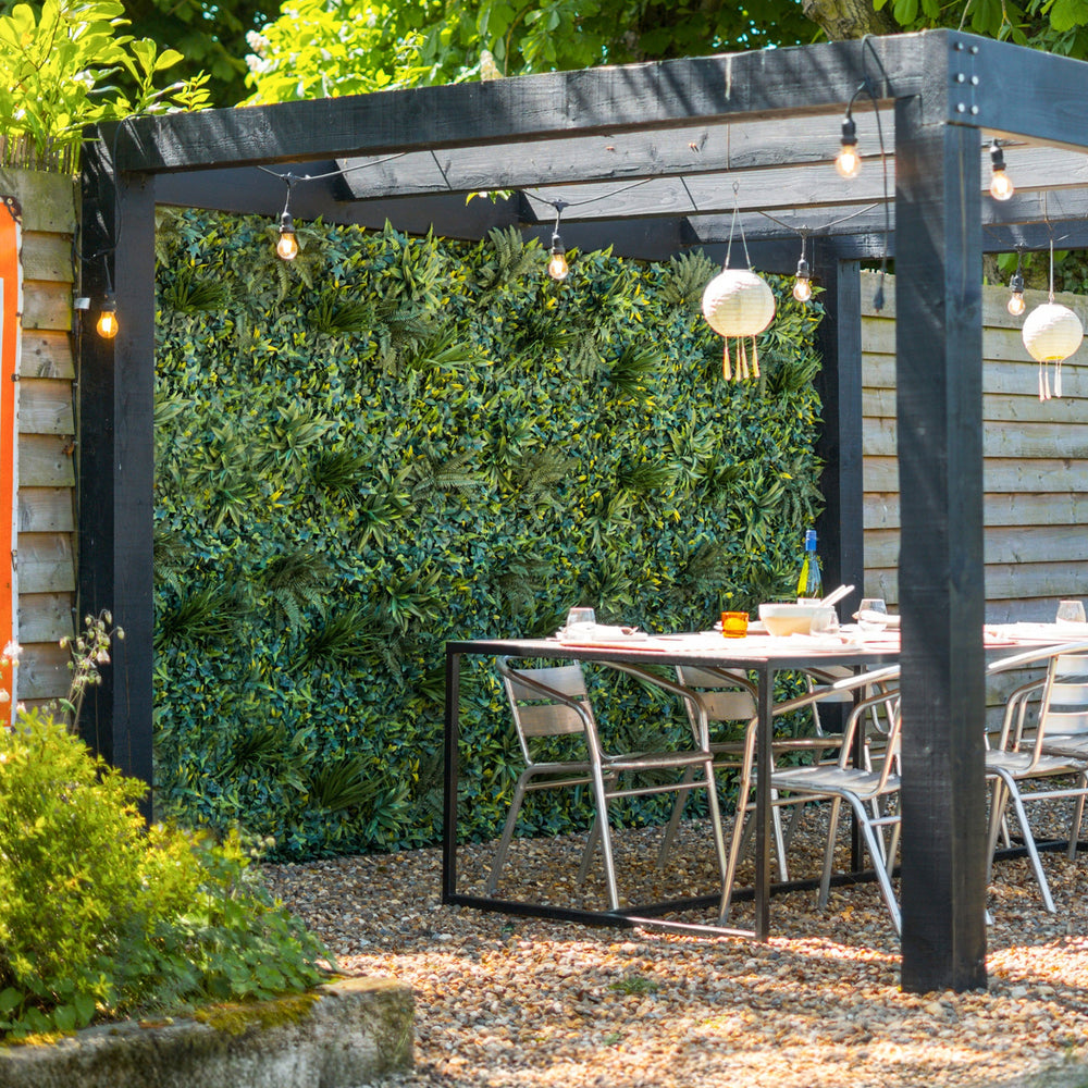 Outdoor patio area with a pergola, table, and chairs surrounded by greenery.