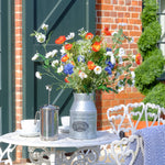 Floral arrangement in a metal vase on a table with a brick building in the background