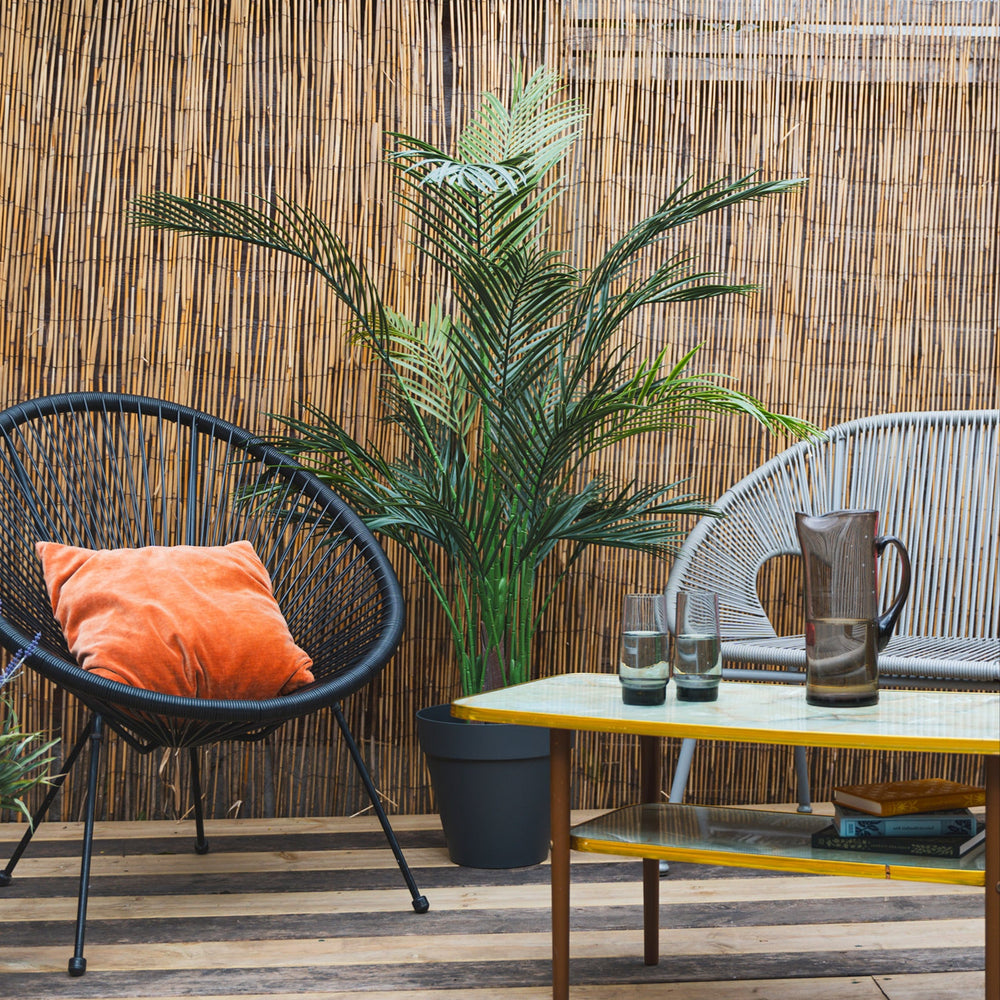 Outdoor patio with wicker chair, table, and plants against a bamboo wall.