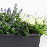 Artificial plants including lavender and white flowers in a black pot on a white background