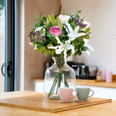 Bouquet of flowers in a clear vase on a wooden table with a kitchen background