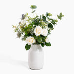 Bouquet of white flowers and greenery in a white vase on a white background