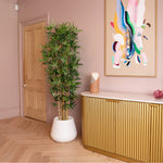 Modern interior with a gold cabinet, white planter with green plant, and colorful abstract art on pink wall.