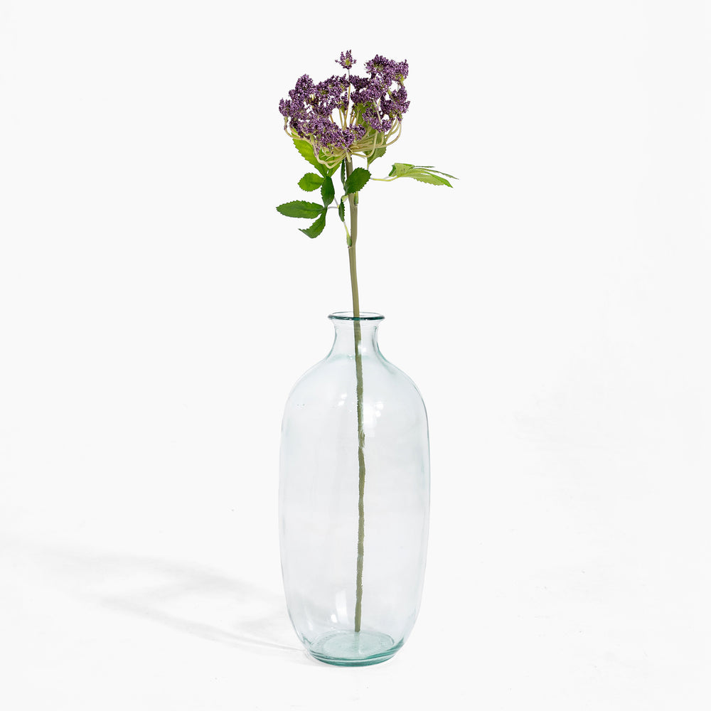 Clear glass bottle with a single stem of purple flowers on a white background