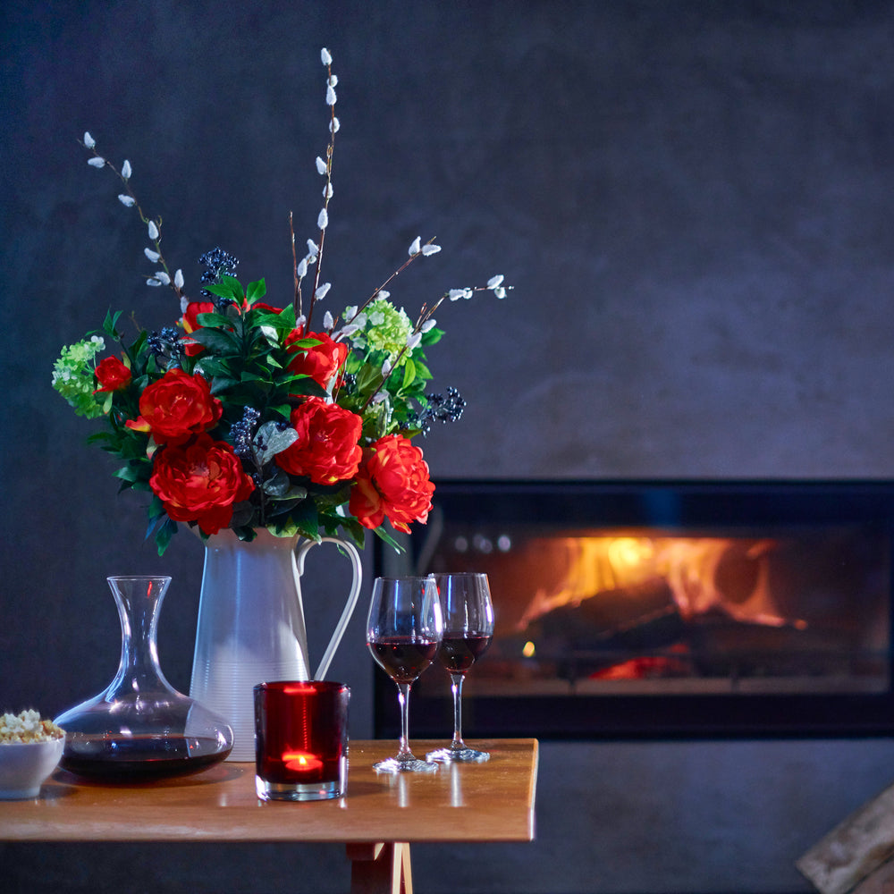Floral arrangement with wine glasses and a candle on a table in front of a fireplace.
