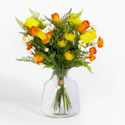 Bouquet of yellow and orange flowers in a clear glass vase on a white background