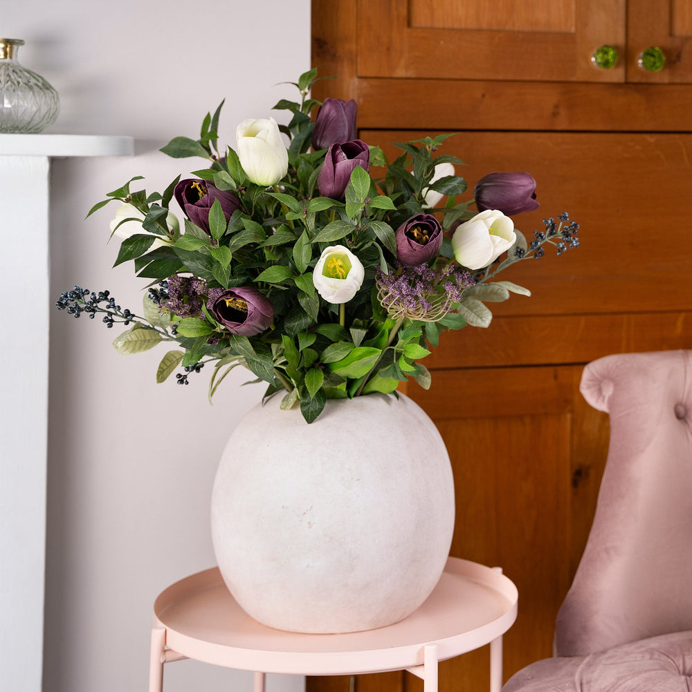 Floral arrangement in a white vase on a small table next to a pink chair.