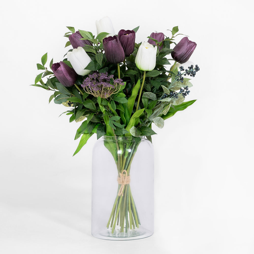 Bouquet of purple and white tulips in a clear glass vase on a white background