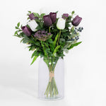 Bouquet of purple and white tulips in a clear glass vase on a white background