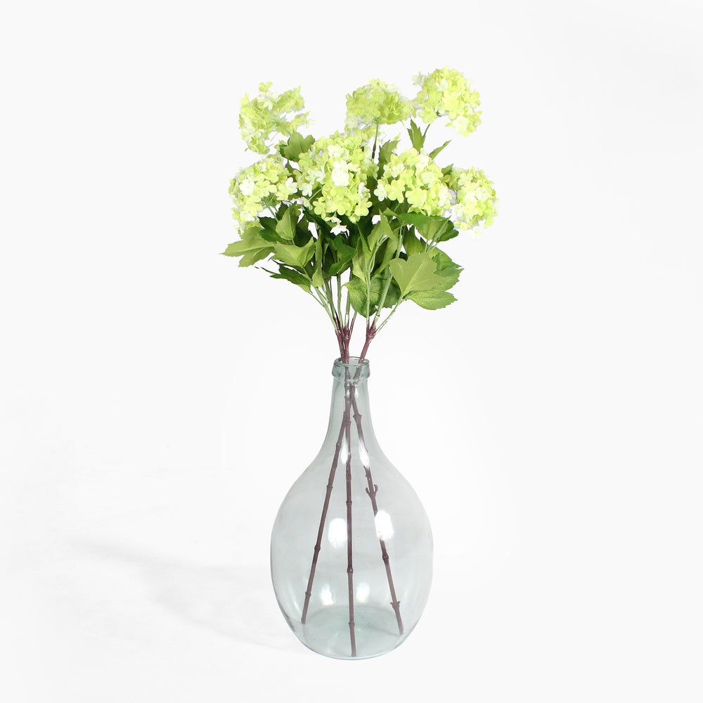 Clear glass vase with green artificial flowers on a white background