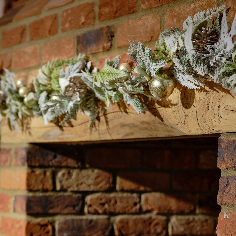 Decorative greenery with gold ornaments on a wooden mantel against a brick wall.