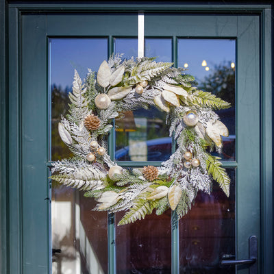 Decorative wreath with greenery and ornaments hanging on a door.
