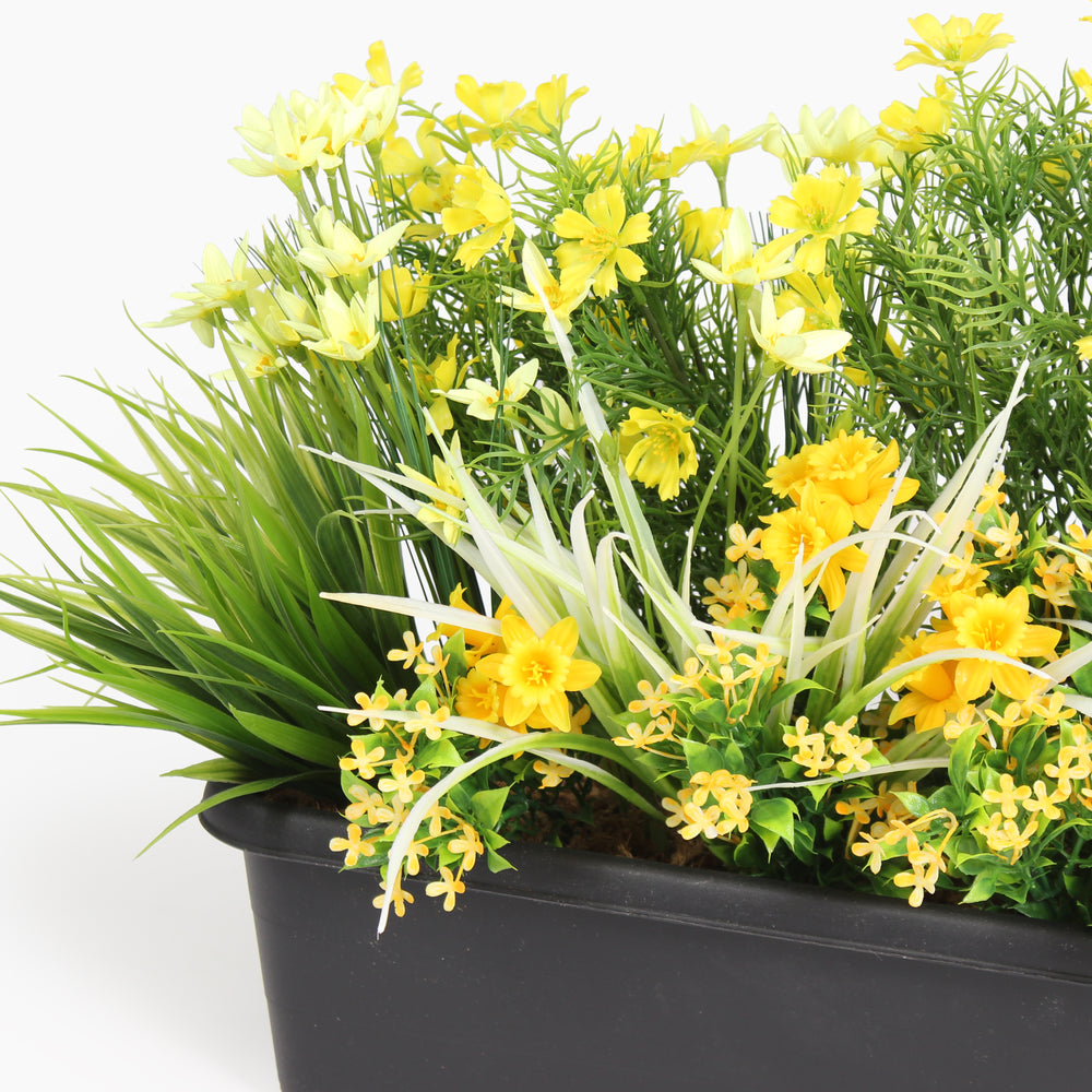 Close up of artificial planter with yellow flowers in a black pot on a white background