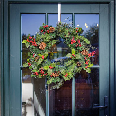 Christmas wreath with greenery, red berries, and pinecones on a glass door.