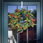Christmas wreath with greenery, red berries, and pinecones on a glass door.