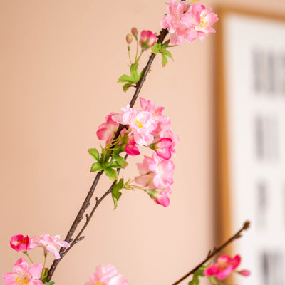 Pink artificial flowers on a branch against a peach wall