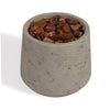A small cylindrical concrete planter with a textured light gray finish, filled with chunky brown bark chips, shown on a white background.