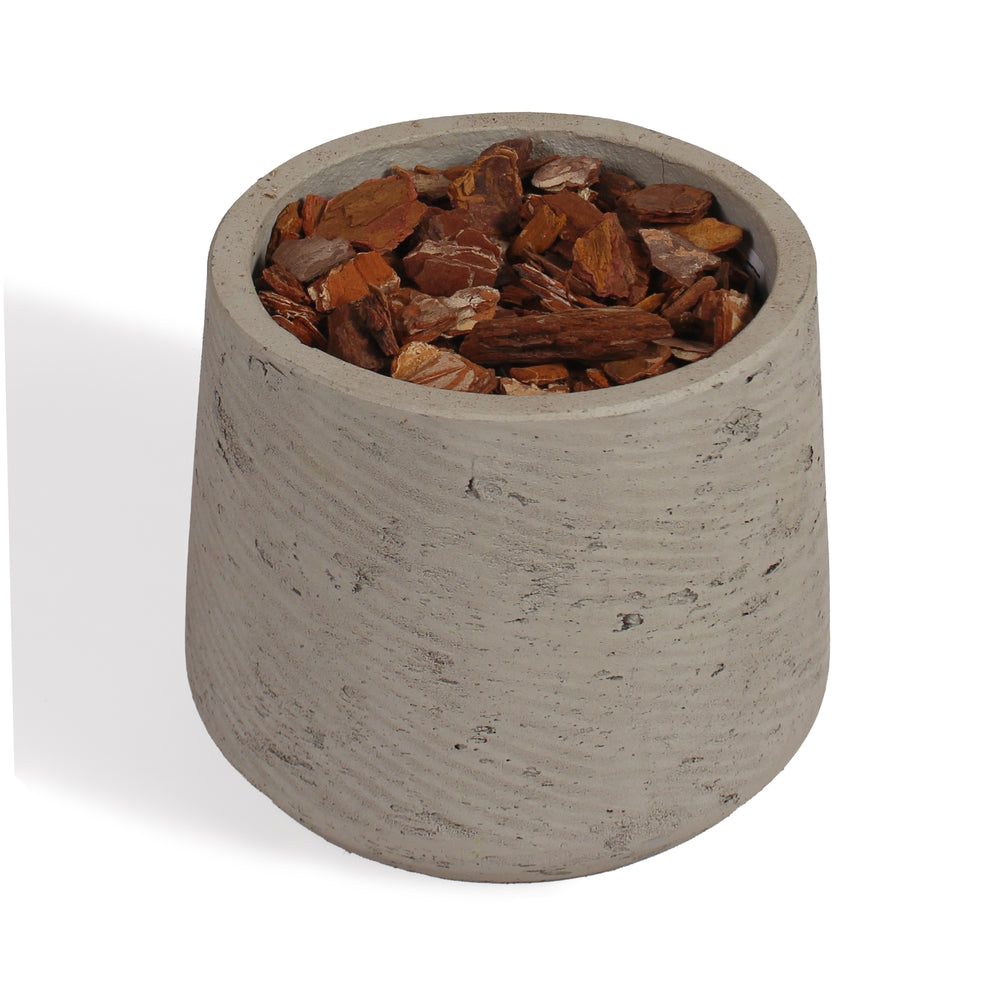 A small cylindrical concrete planter with a textured light gray finish, filled with chunky brown bark chips, shown on a white background.