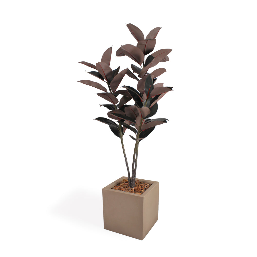 An artificial potted plant with dark reddish-brown leaves in a square beige planter topped with brown bark, shown on a plain white background.
